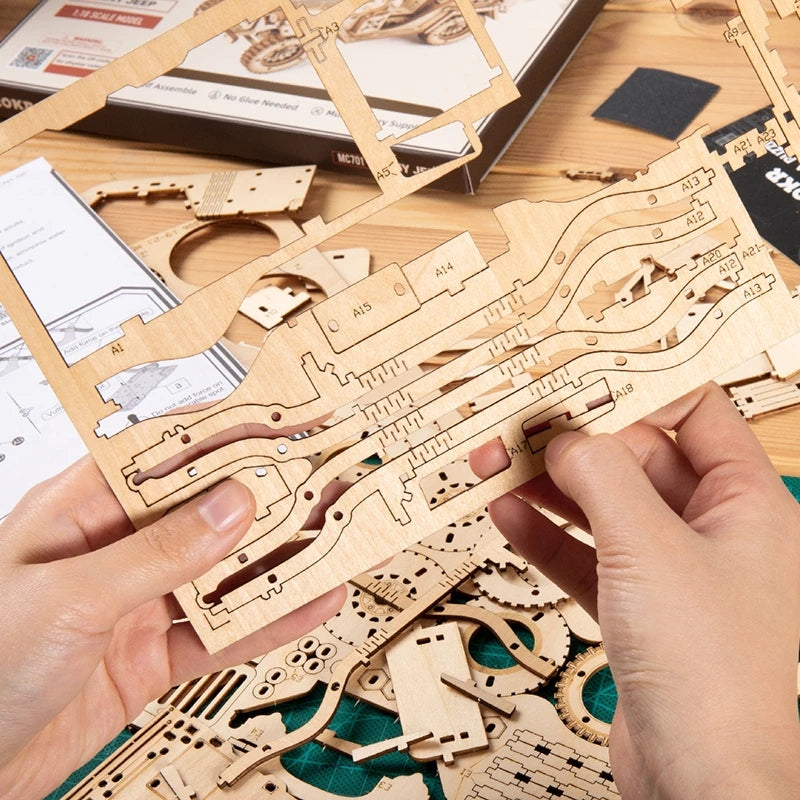Wooden mechanical model kit with hands assembling pieces on a wooden table.