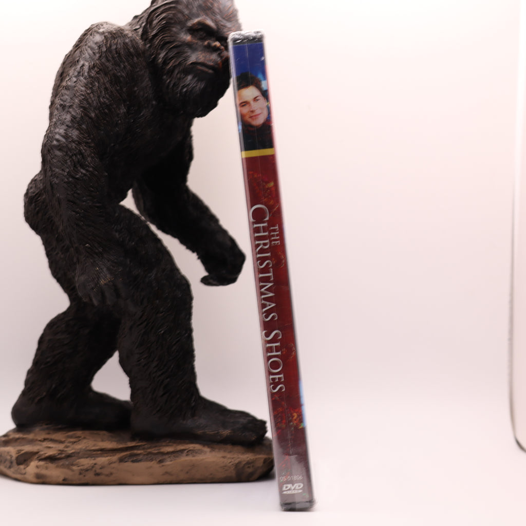 Statue of a bigfoot next to a DVD case titled 'The Christmas Shoes' on a white background