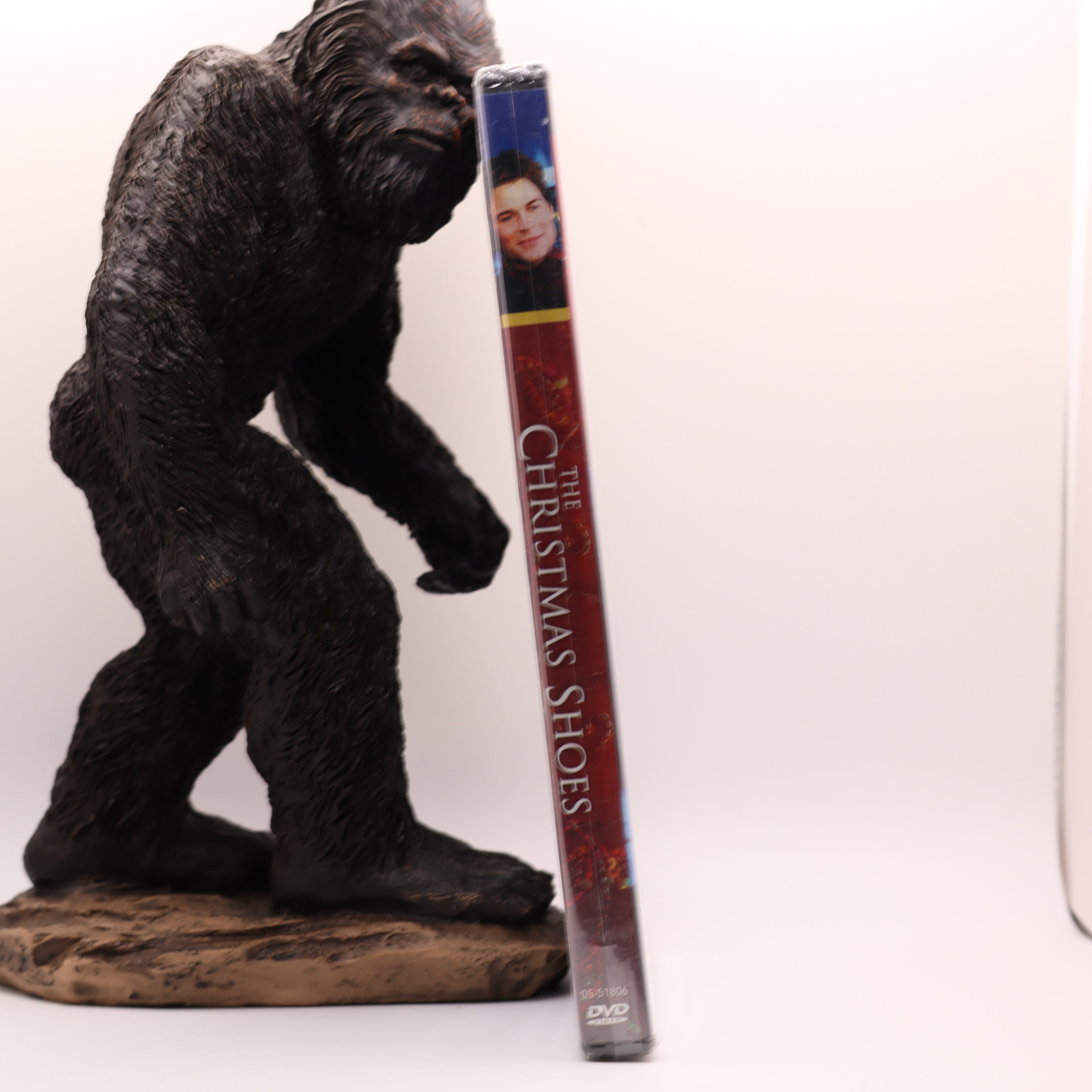 Statue of a bigfoot next to a DVD case titled 'The Christmas Shoes' on a white background