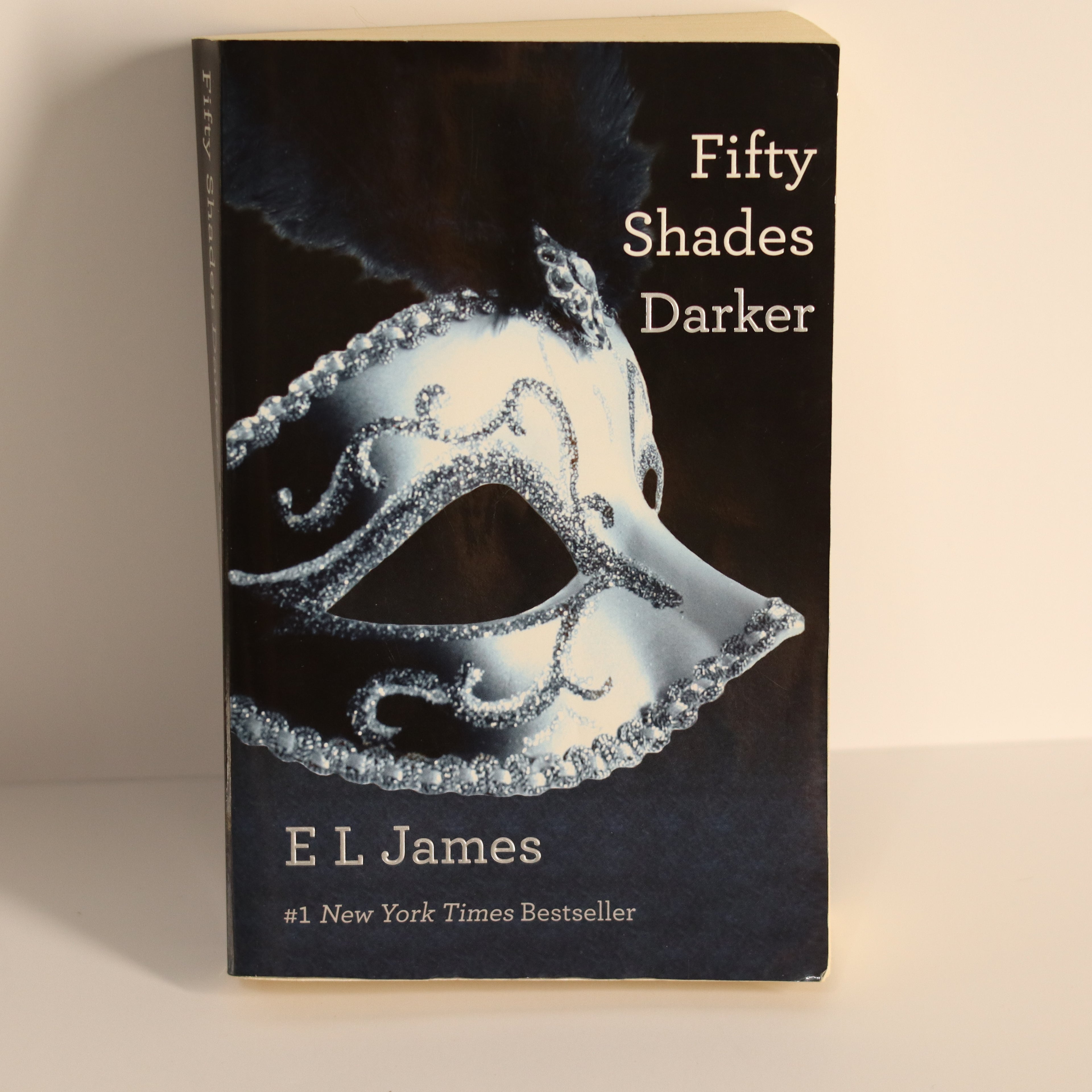 Book titled 'Fifty Shades Darker' by E L James with a black cover and silver mask design.