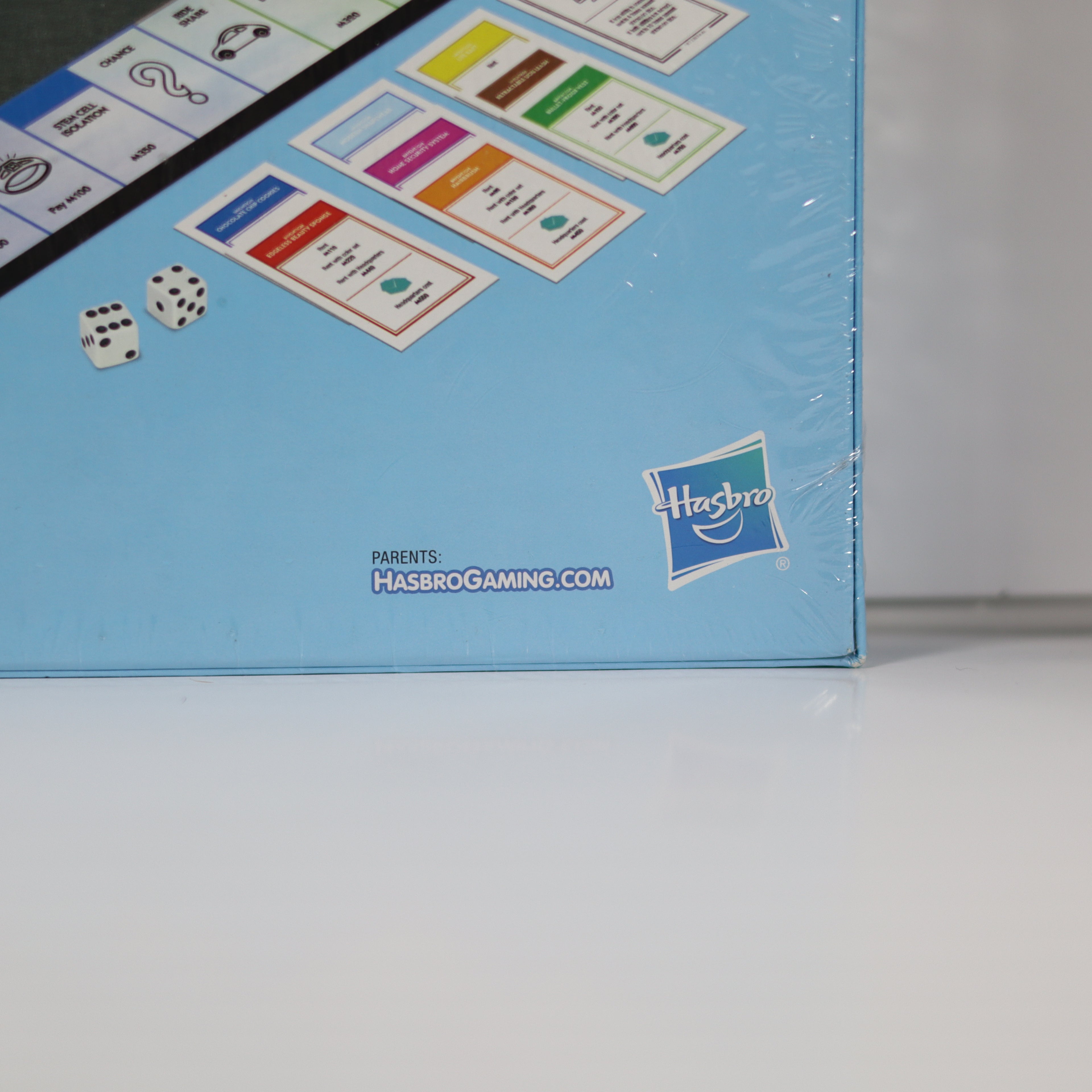 Close-up of a Hasbro gaming box with cards and dice on a light blue background.