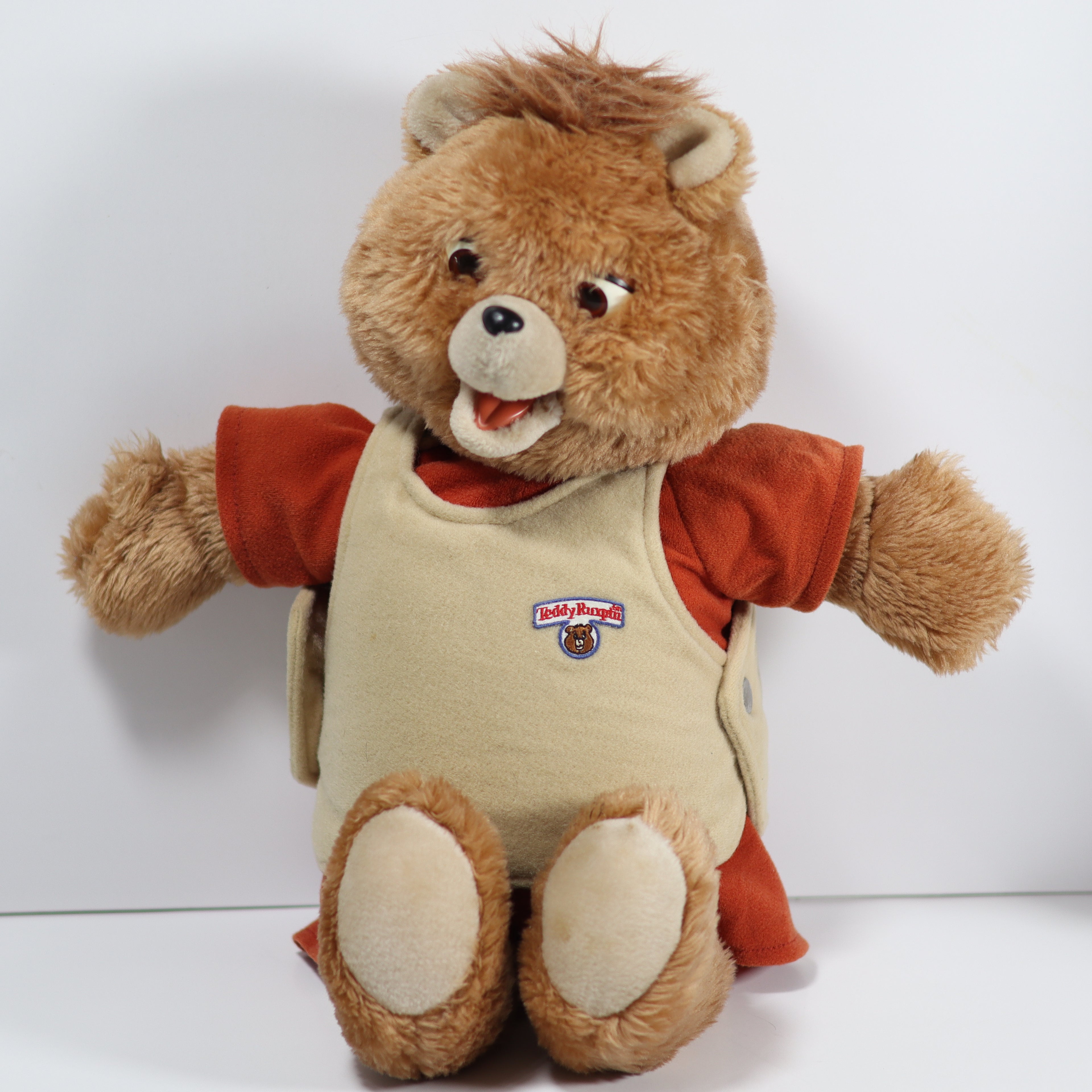 Plush teddy bear with a red shirt and beige apron on a white background