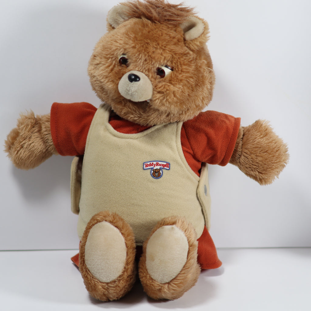 Plush bear wearing a red shirt and beige apron with a logo on a white background