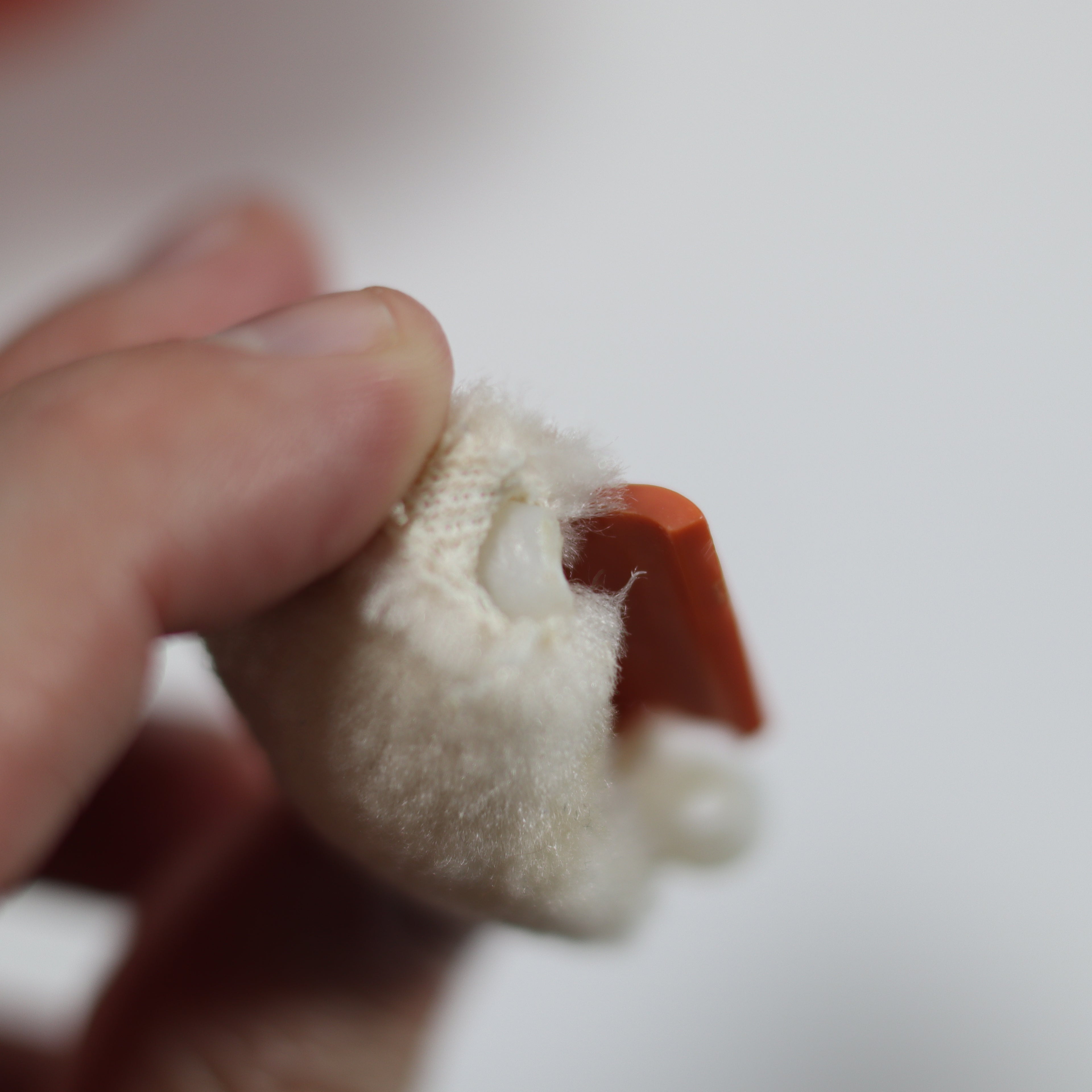 Close-up of a hand holding a small white object with a red base against a blurred background
