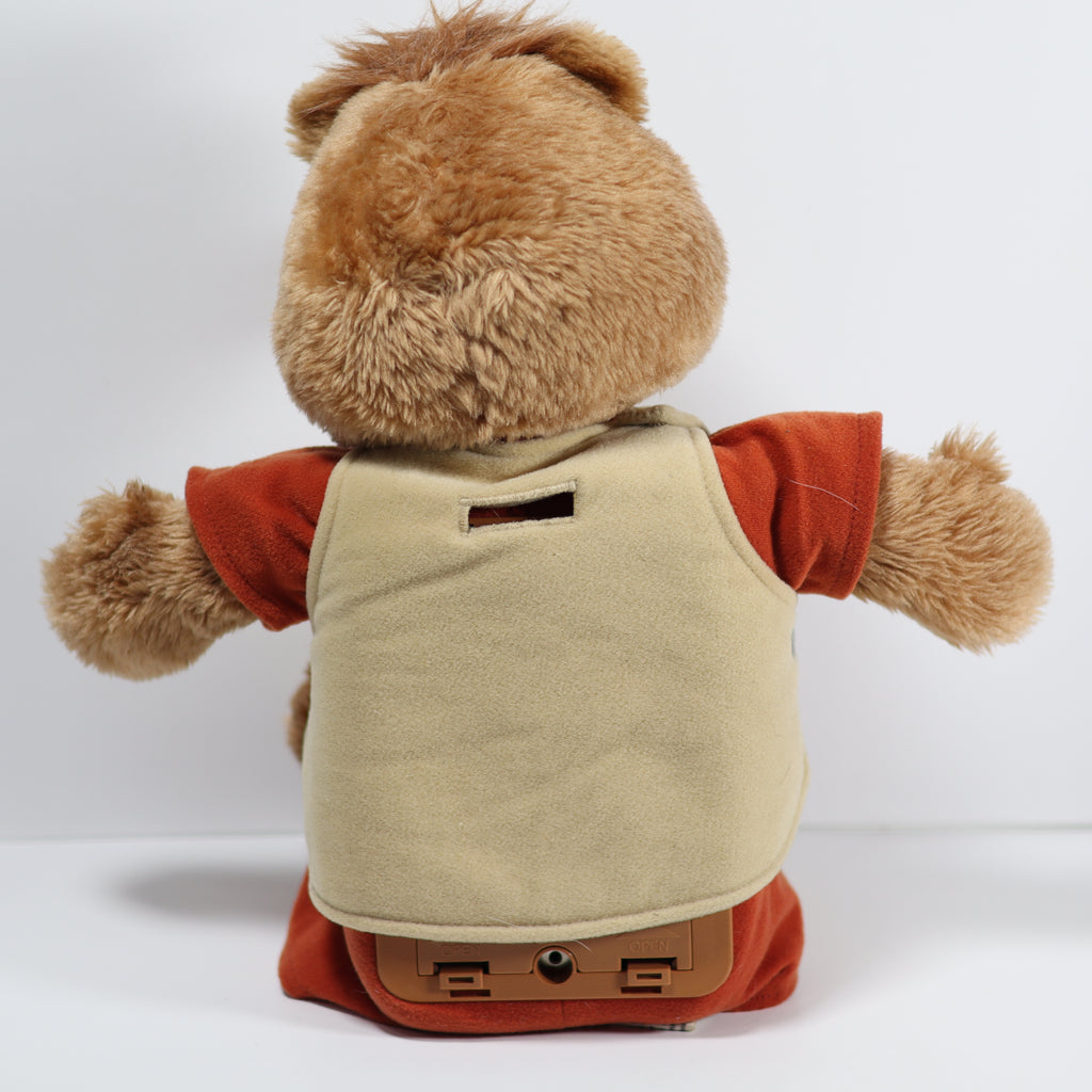 Plush bear toy with a beige vest and red shirt on a white background