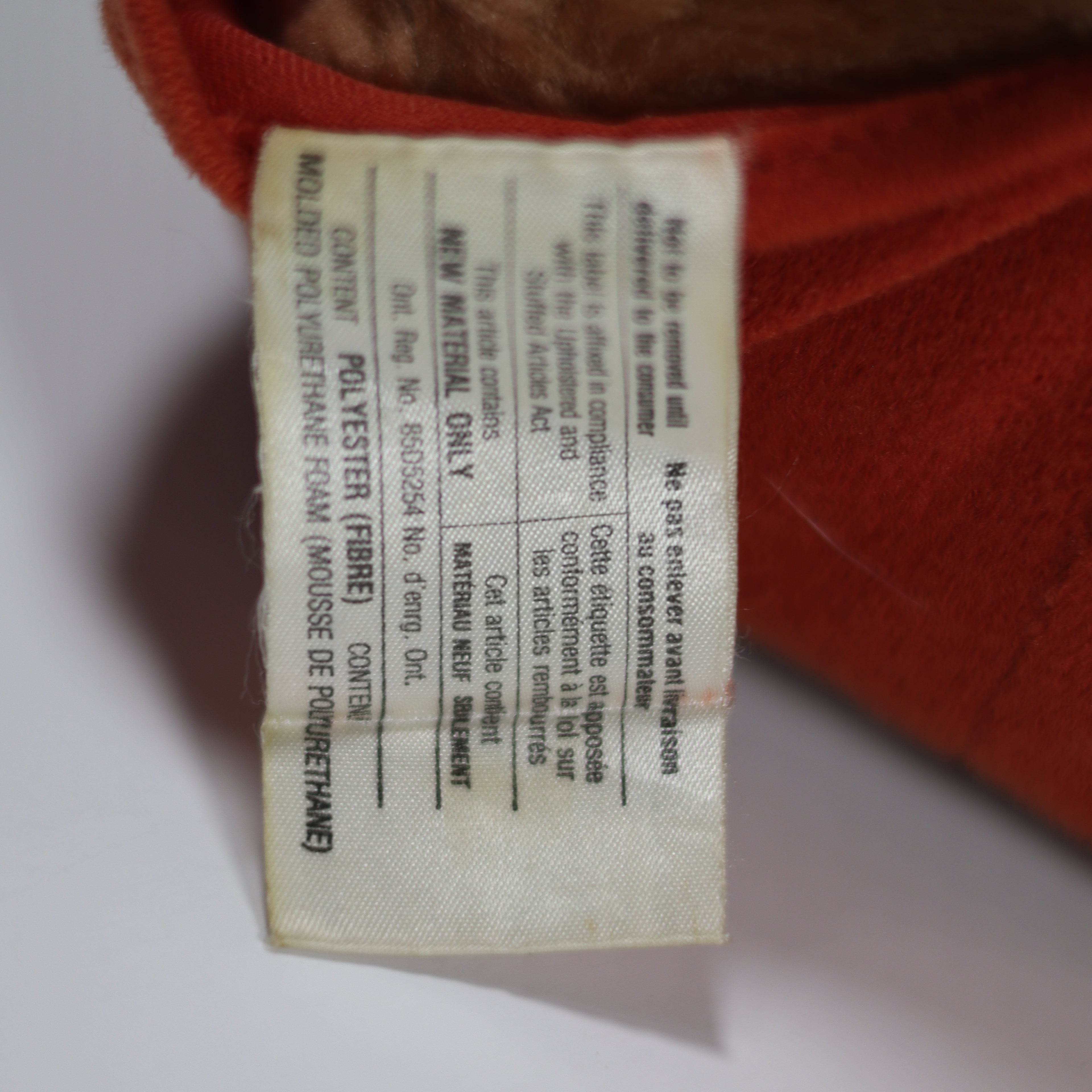 Close-up of a label on a red plush toy with text in multiple languages.
