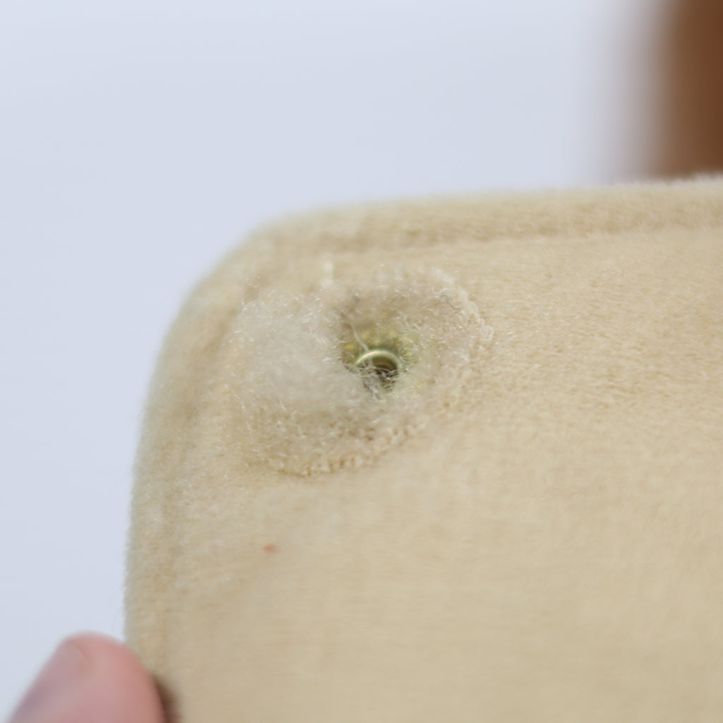 Close-up of a beige fabric item with a hole, held by a hand against a white background.