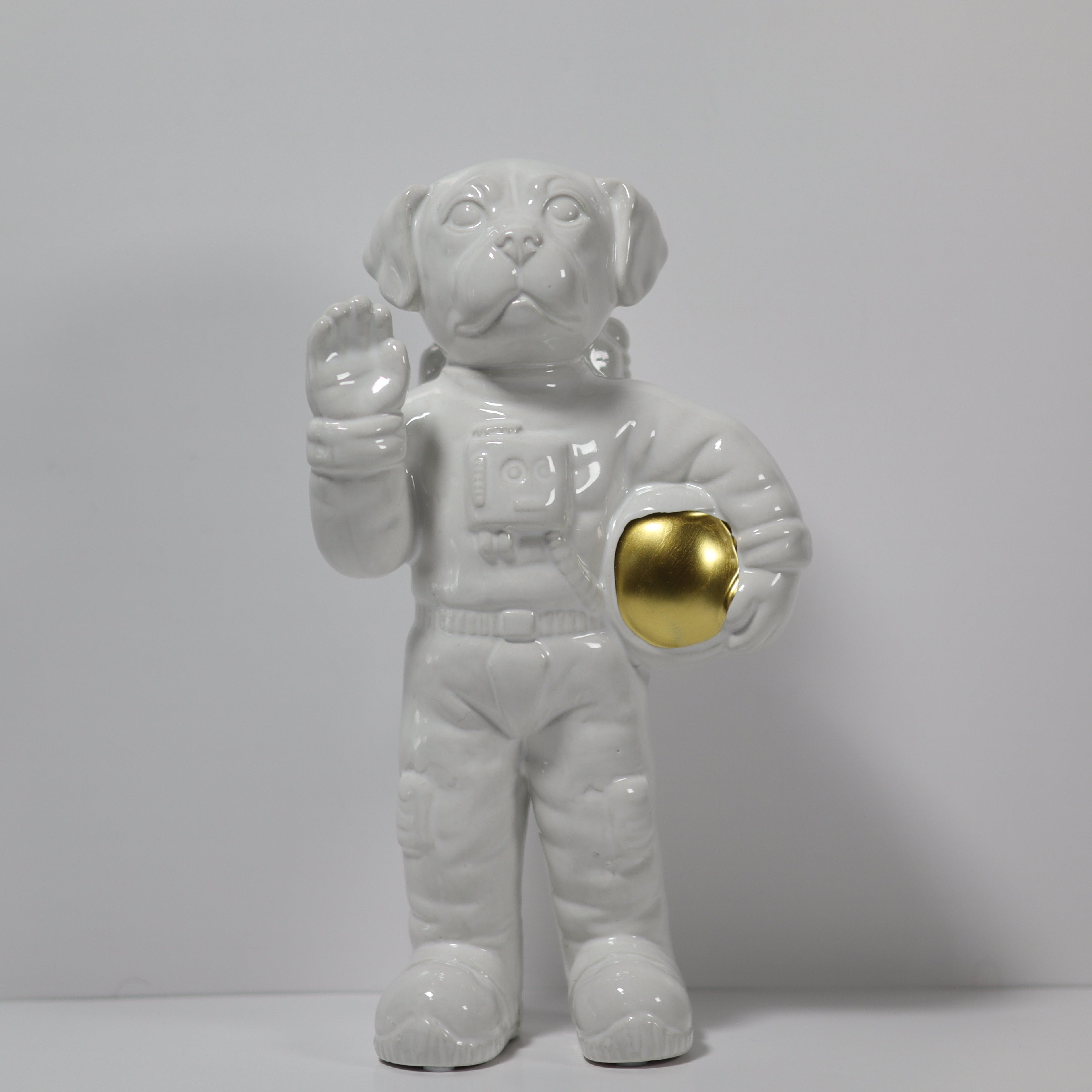 White ceramic dog figurine in astronaut costume with gold ball on gray background