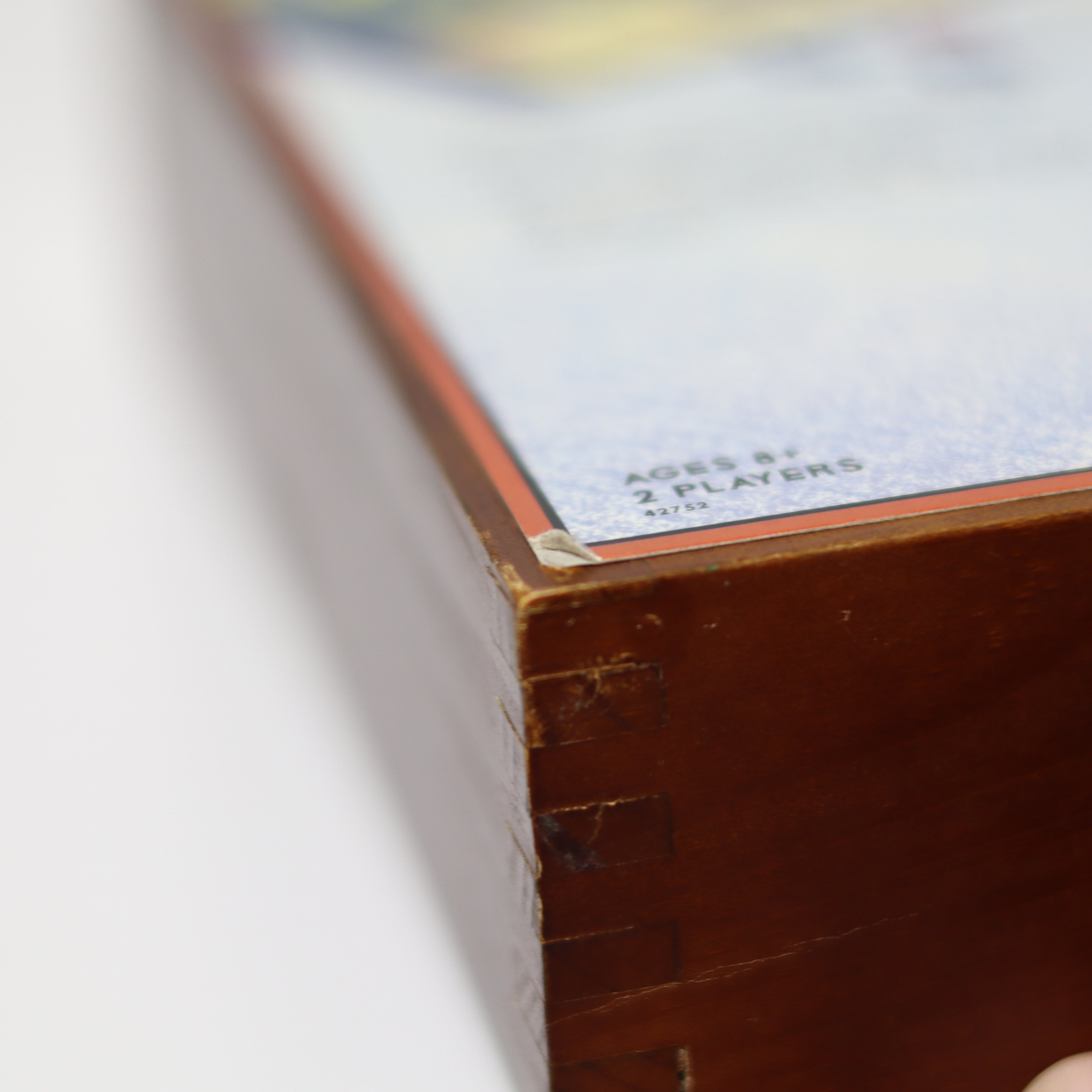 Close-up of a wooden game box corner with text on a white background