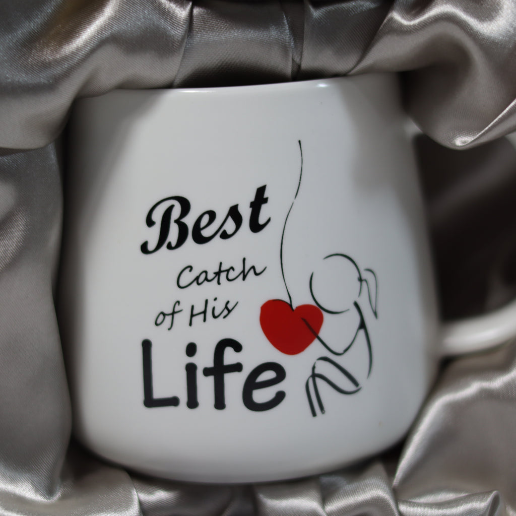 White mug with 'Best Catch of His Life' text and red heart on silver fabric