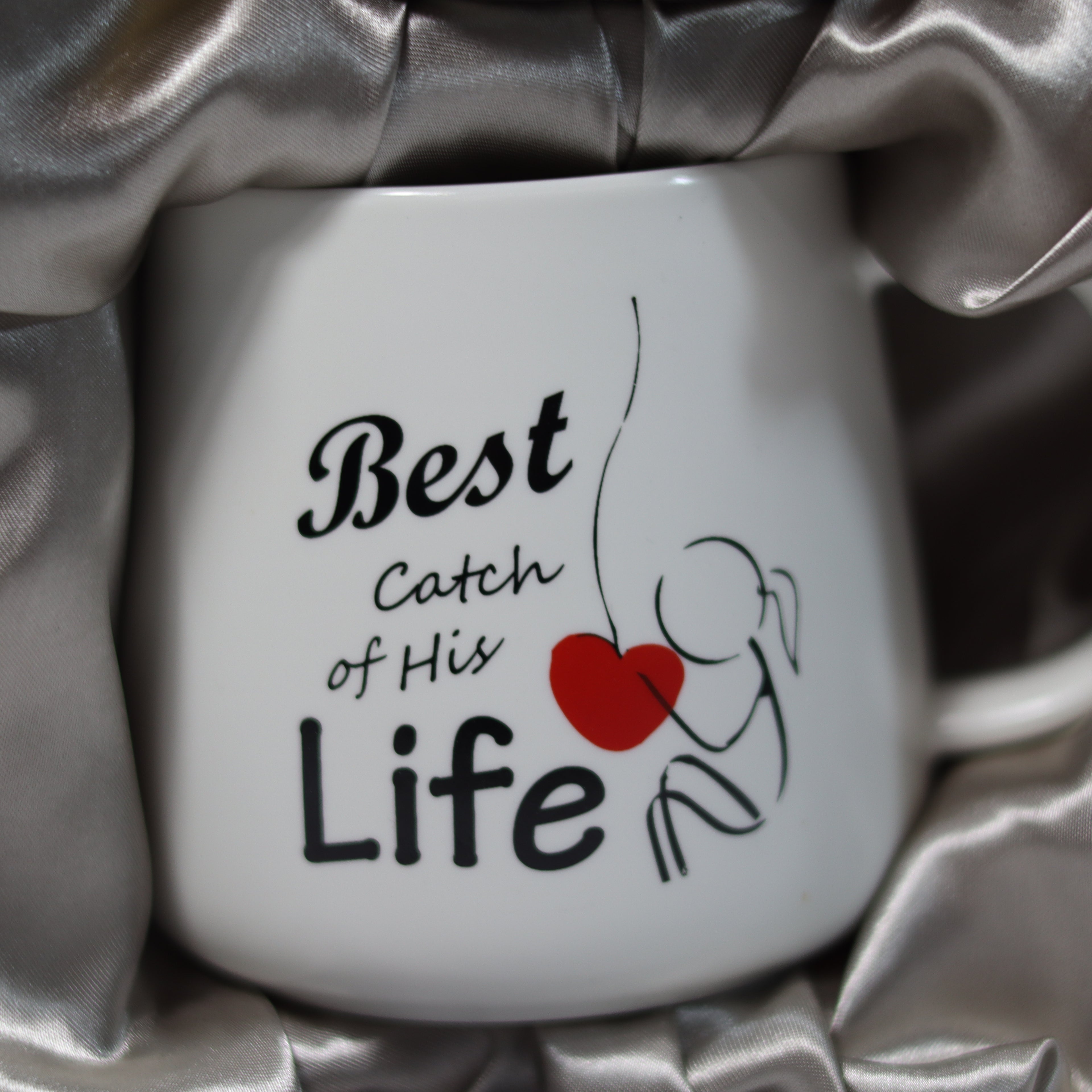 White mug with 'Best Catch of His Life' text and red heart on silver fabric