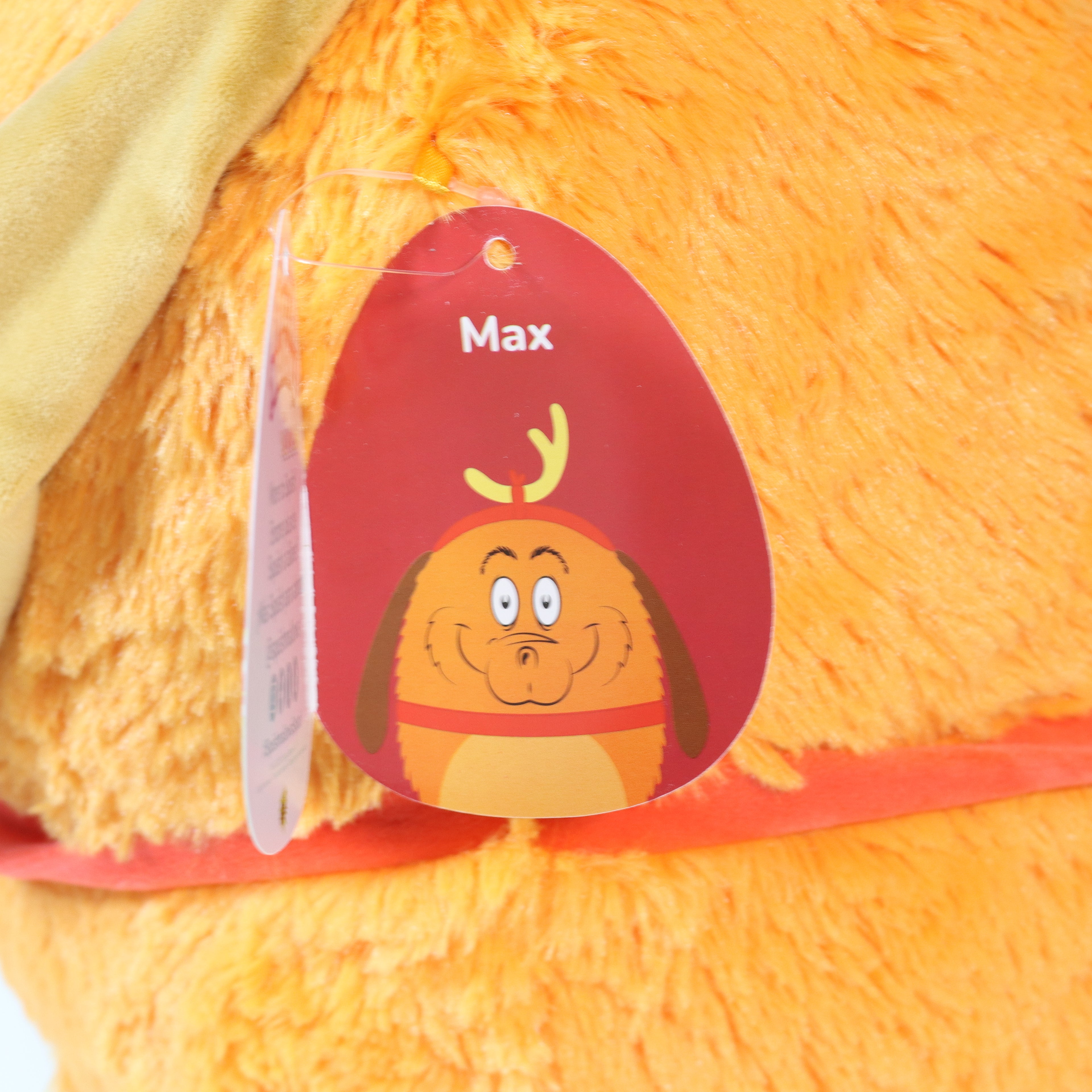 Close-up of a plush toy with a name tag labeled 'Max' on an orange background.