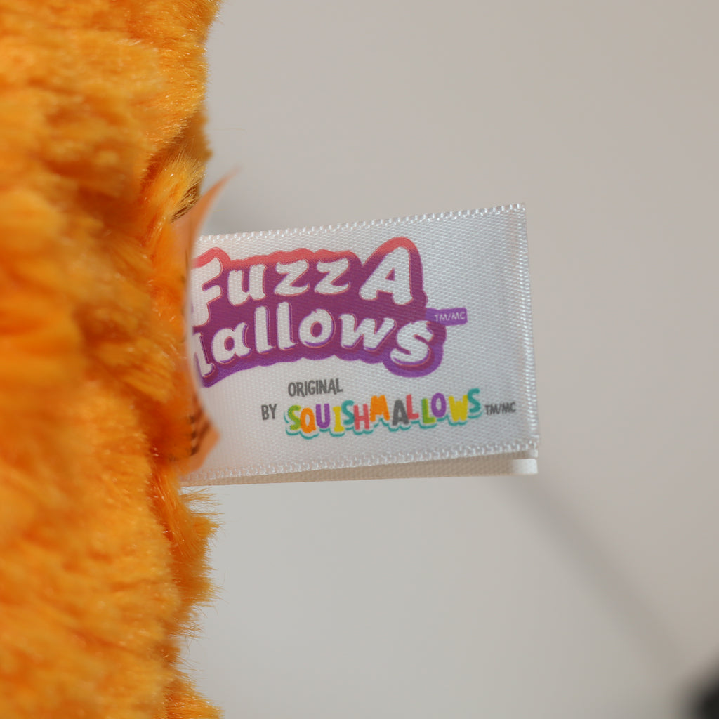 Close-up of an orange plush toy with a 'Fuzz A Mallovs' label on a white background