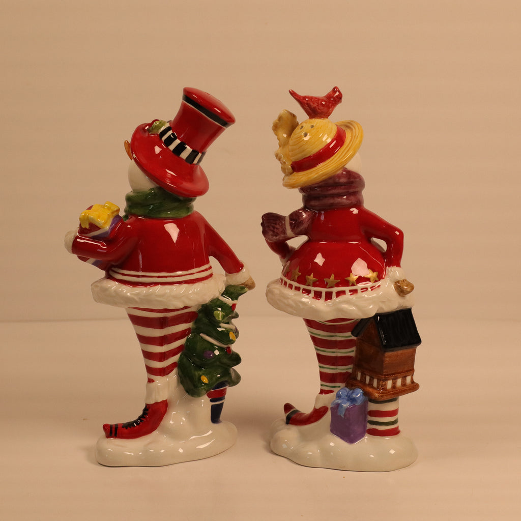 Two ceramic figures of people in festive outfits with hats and striped outfits on a plain background.