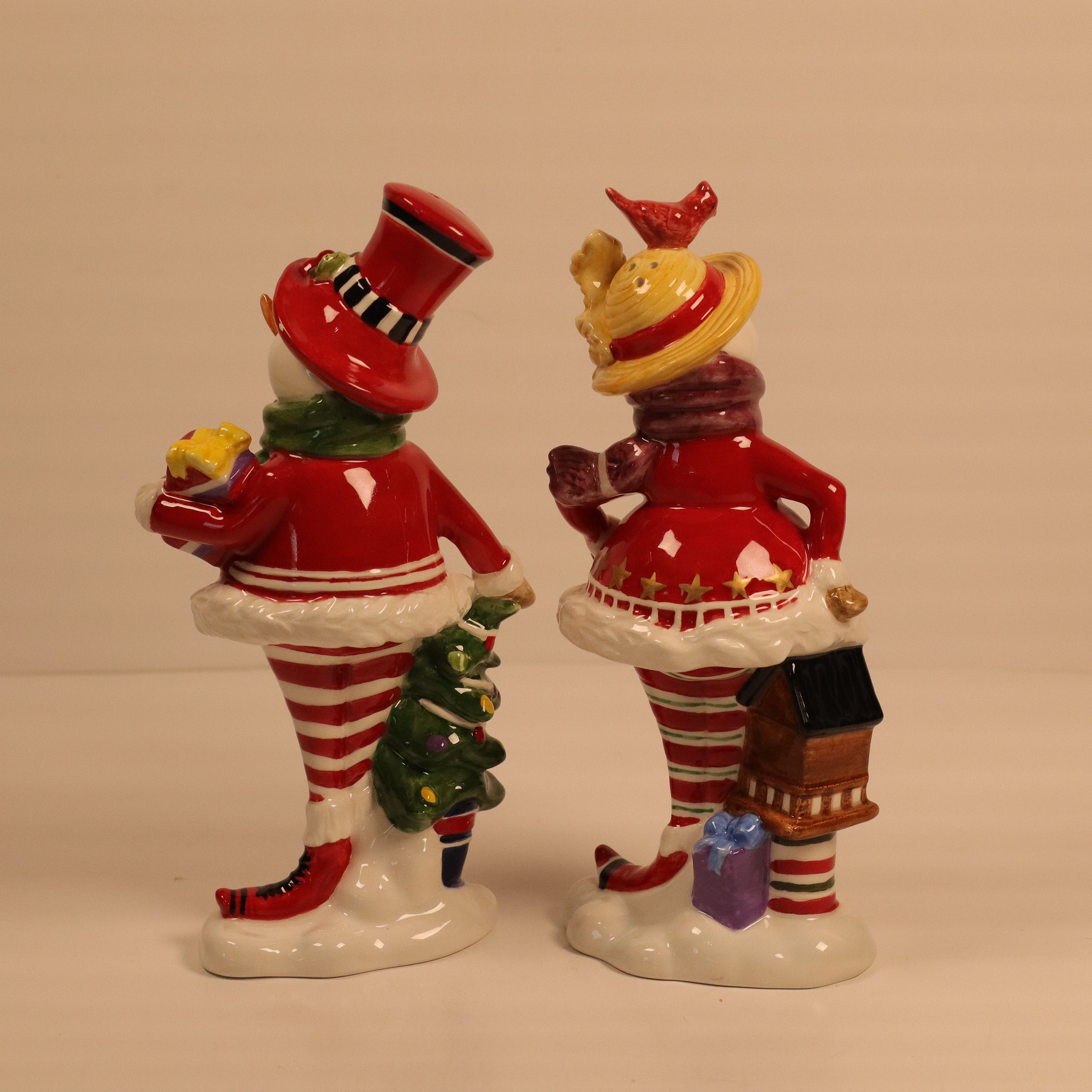 Two ceramic figures of people in festive outfits with hats and striped outfits on a plain background.