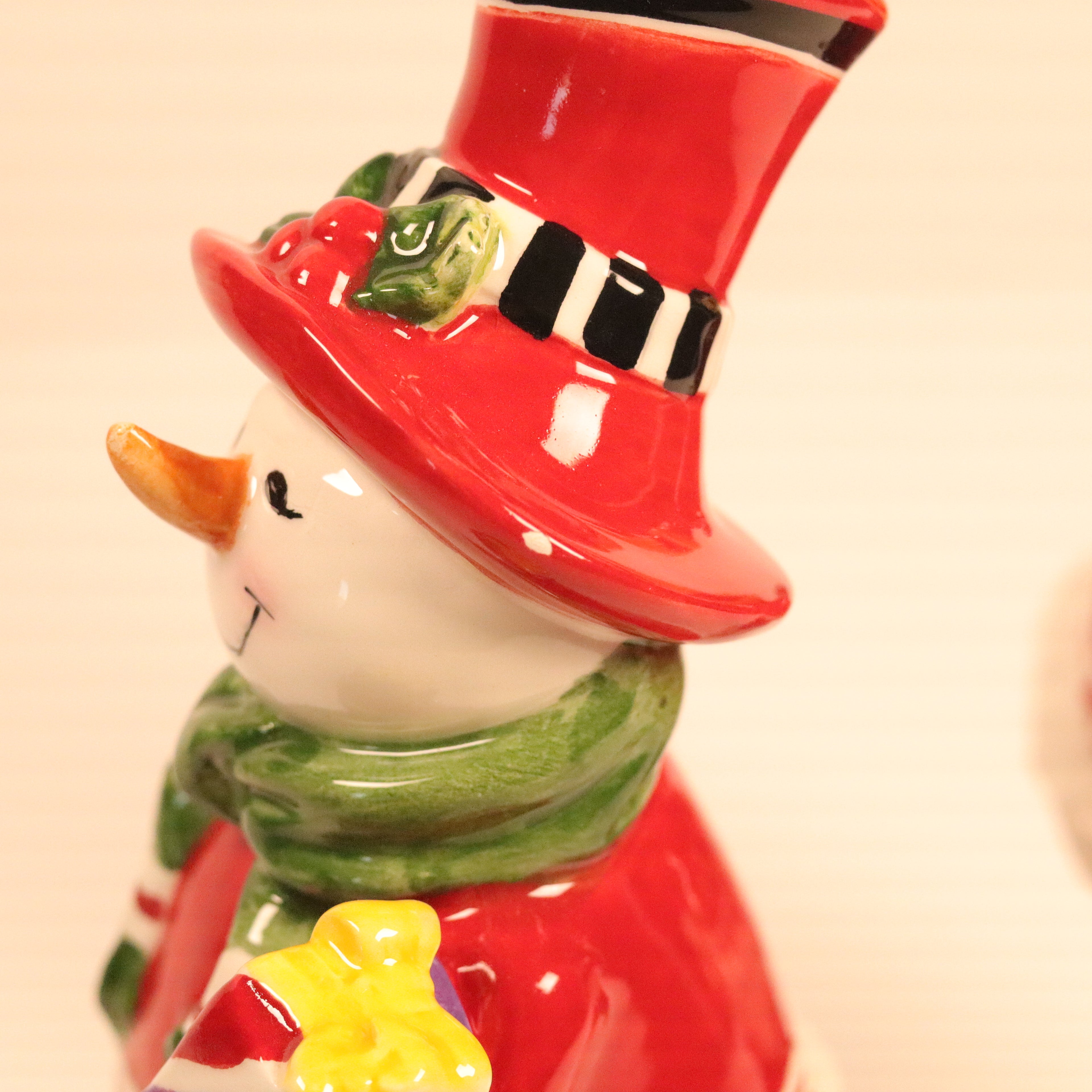 Ceramic snowman figurine with a red hat and green scarf on a beige background