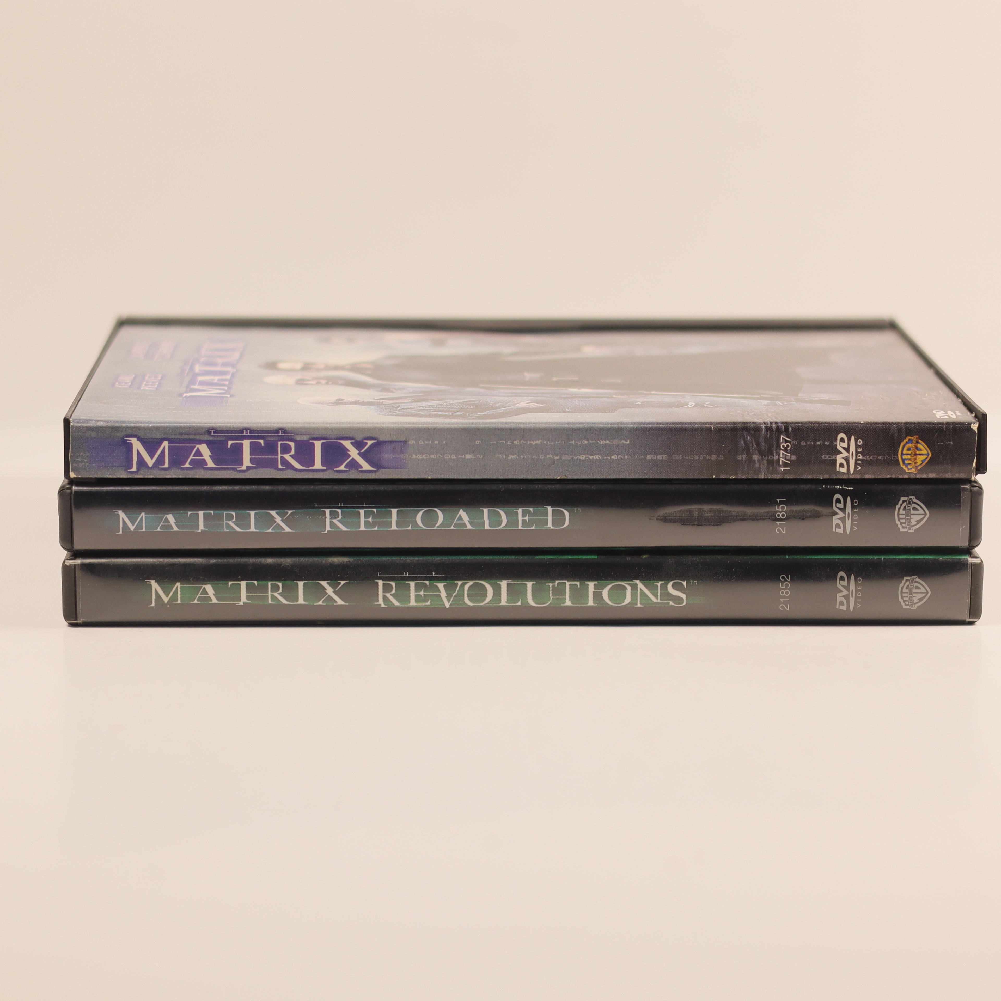 Three DVDs titled 'Matrix', 'Matrix Reloaded', and 'Matrix Revolutions' stacked on a beige background.