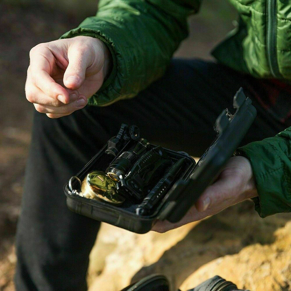 Person holding a black case with items inside, outdoors.